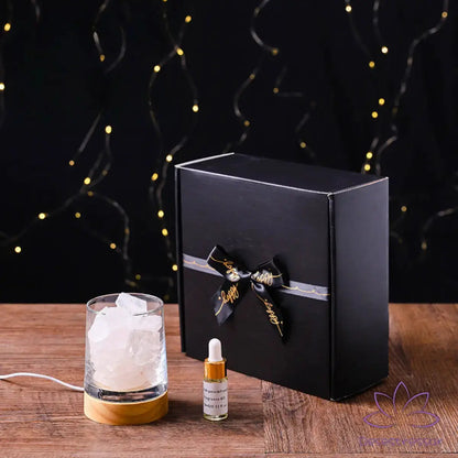 Difusor de aromaterapia AromaLuz com base de madeira, cristal branco iluminado e óleo essencial ao lado, em um ambiente aconchegante.