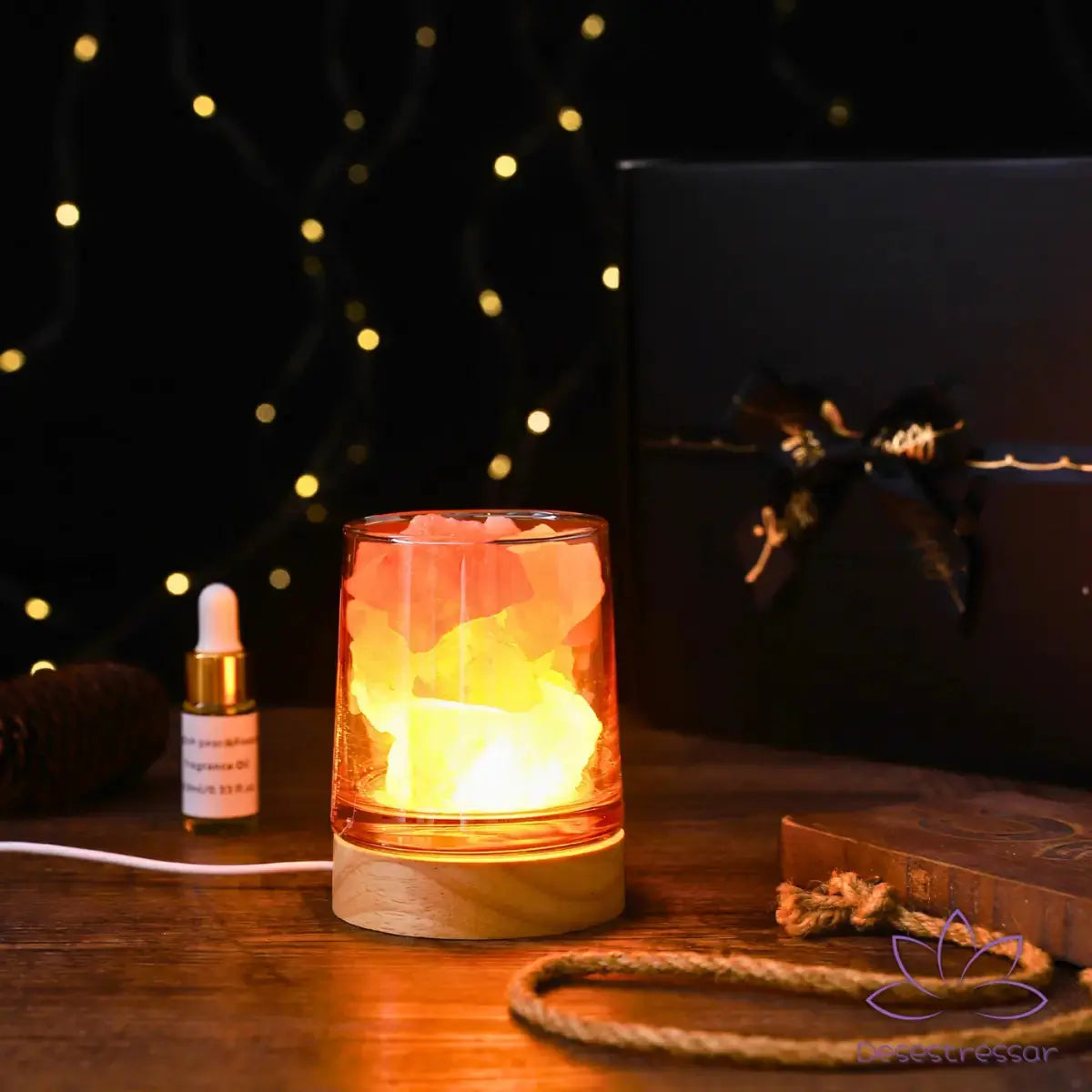 Difusor de aromaterapia AromaLuz com base de madeira, cristal branco iluminado e óleo essencial ao lado, em um ambiente aconchegante.