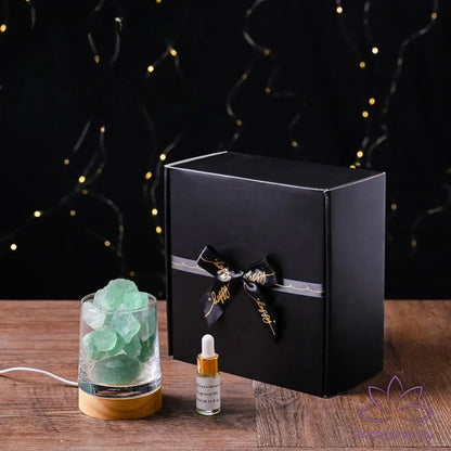 Difusor de aromaterapia AromaLuz com base de madeira, cristal branco iluminado e óleo essencial ao lado, em um ambiente aconchegante.
