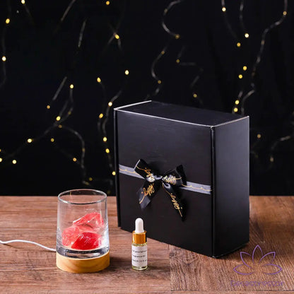Difusor de aromaterapia AromaLuz com base de madeira, cristal branco iluminado e óleo essencial ao lado, em um ambiente aconchegante.